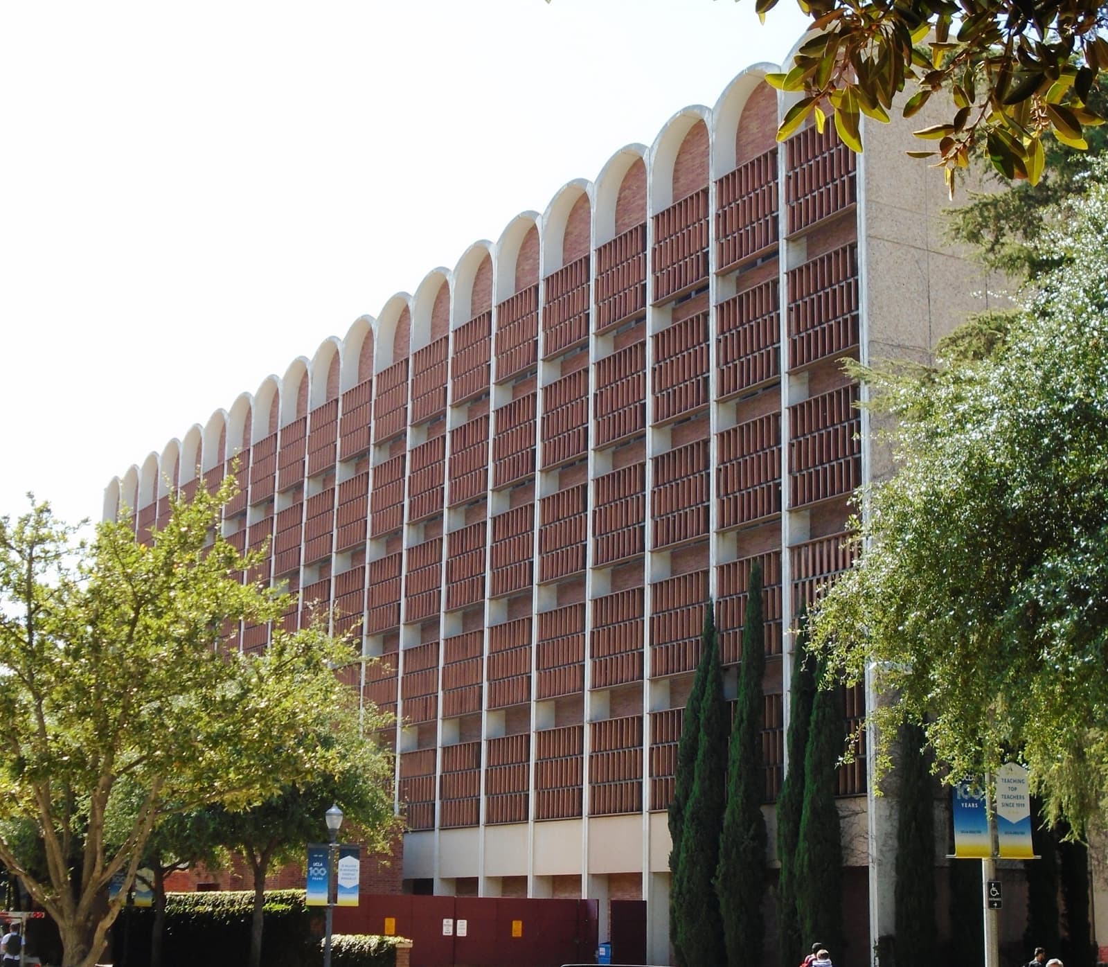 A tall brick building with a scalloped concrete crown among trees