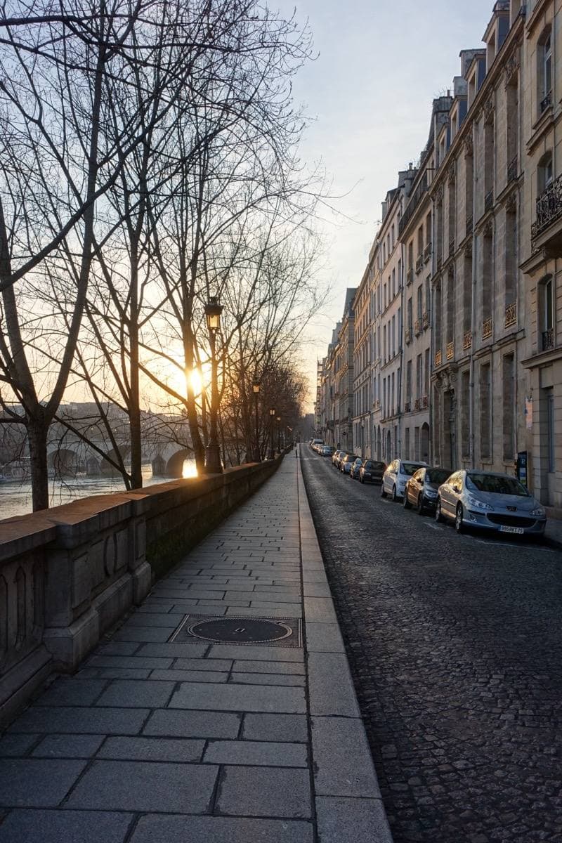 A stone quay with old townhouses on one side and the river wall on the other, low sun