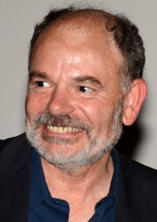 Jean-Pierre Darroussin, grey beard, smiling, in a dark shirt