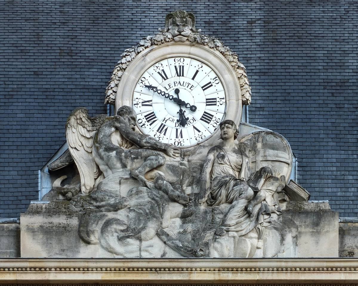 A carved stone clock with sculpted figures against a blue roof