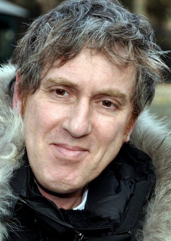 Éric Rochant, grey curly hair, in a dark coat with a fur-trimmed hood