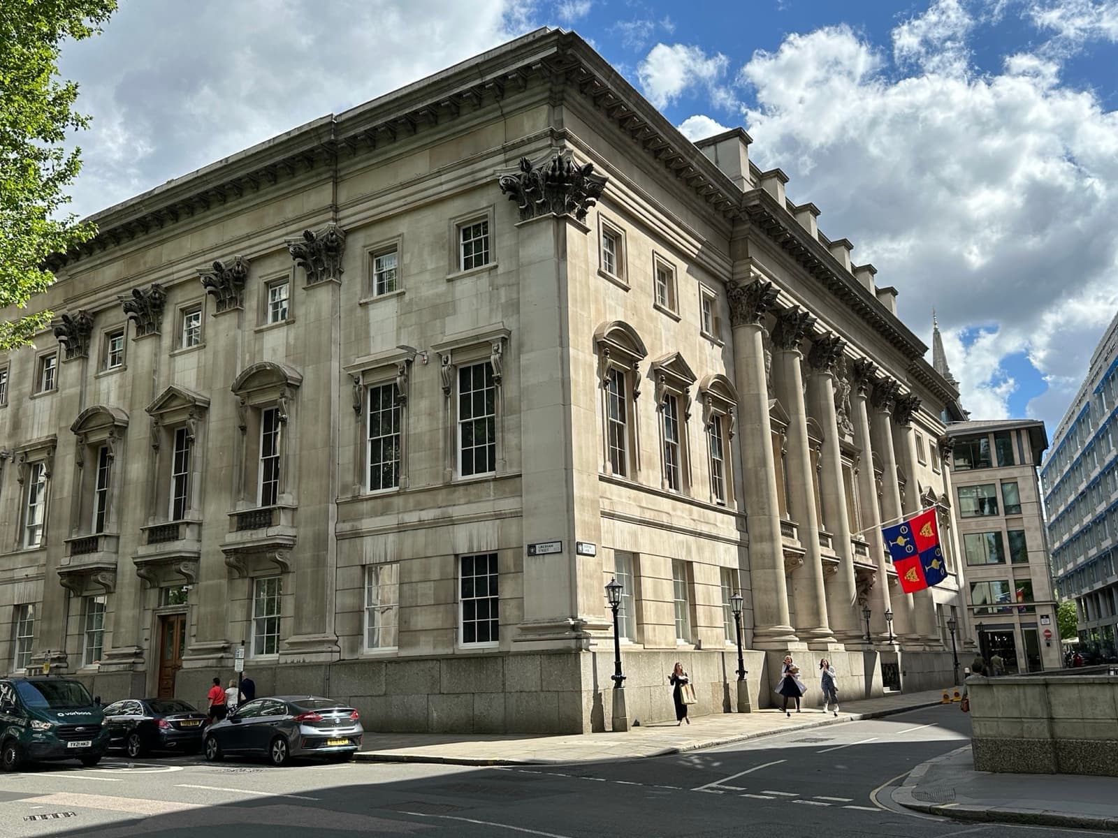 A grey stone hall with tall columns and a flag on a corner of a City street