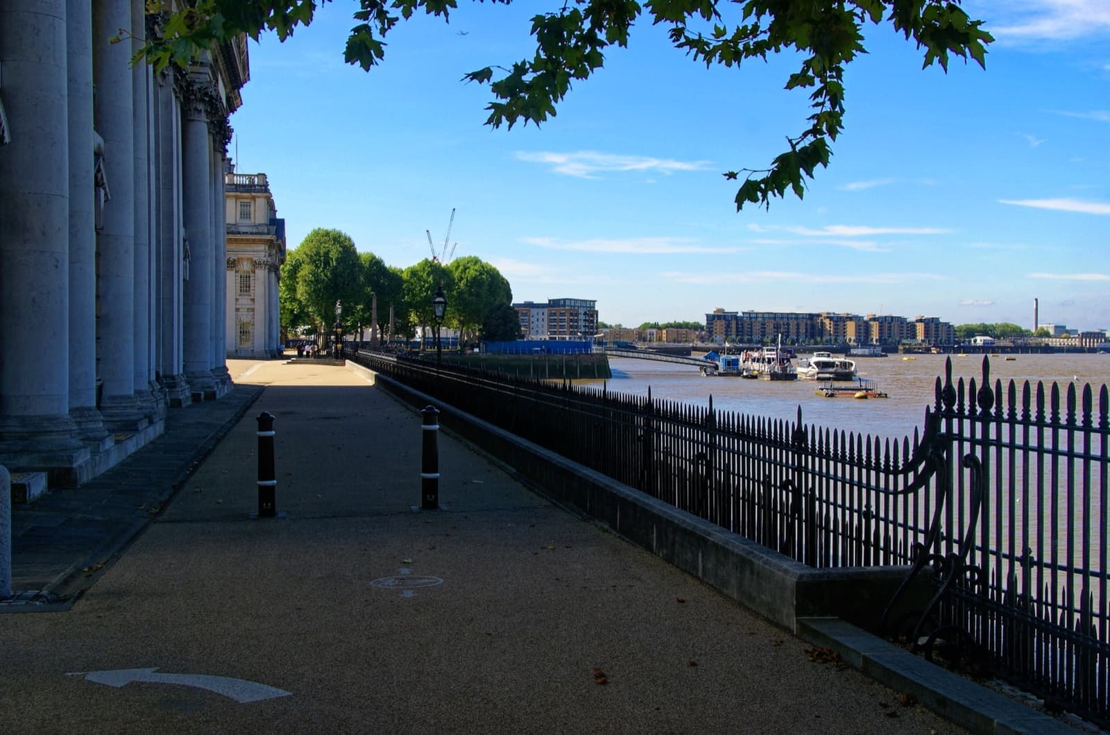 A colonnade and iron railings along the Thames at Greenwich, with a stone terrace in sunlight