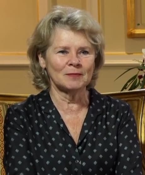Imelda Staunton with short fair hair in a dark spotted blouse, in a gilded room