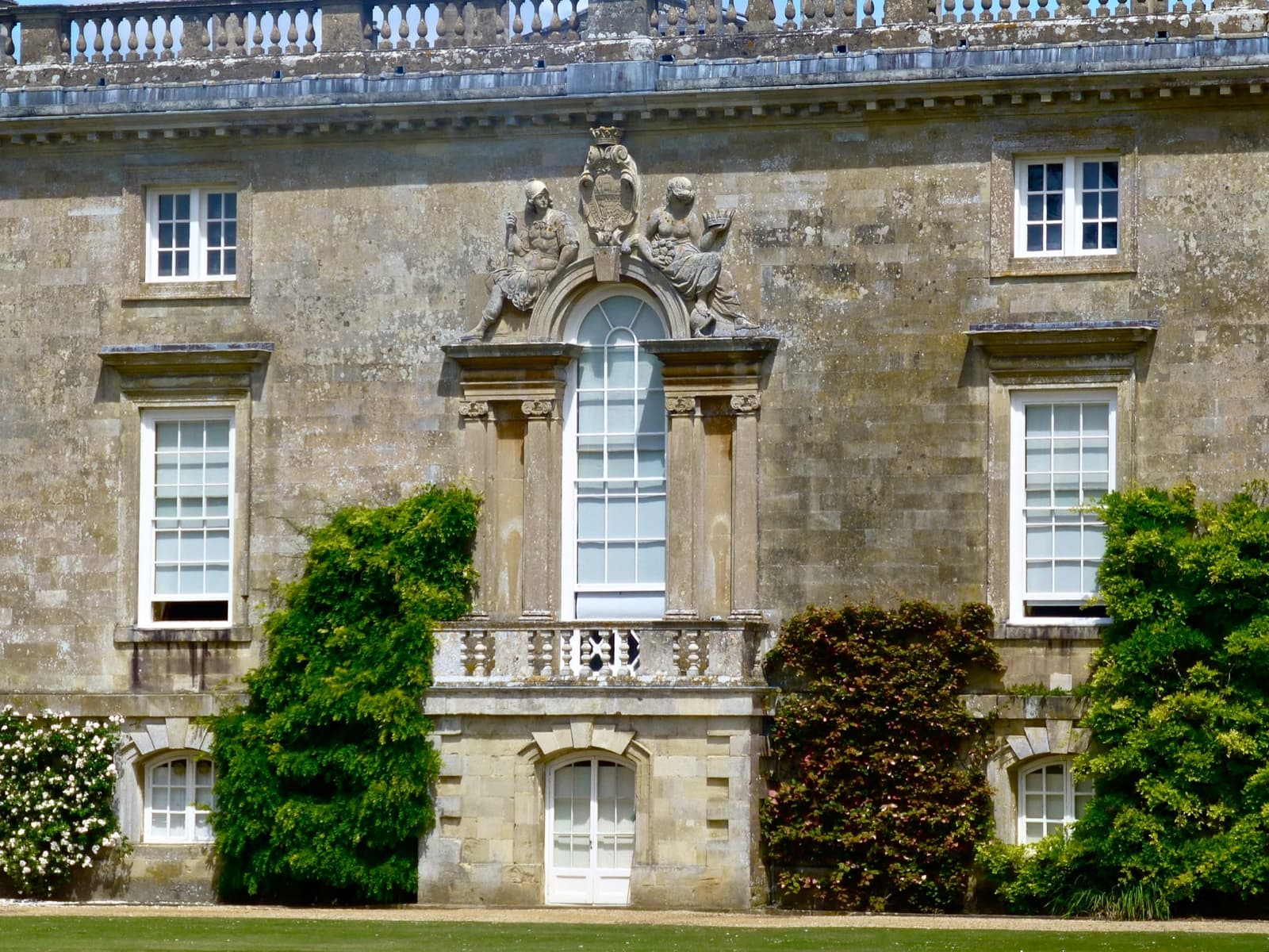 The honey-coloured stone south front of Wilton House with a central Venetian window above a balustrade, and climbing plants