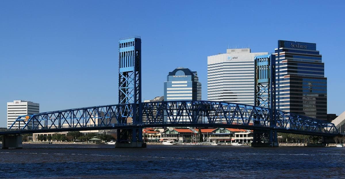 A blue lift bridge over a wide river with the Jacksonville skyline behind