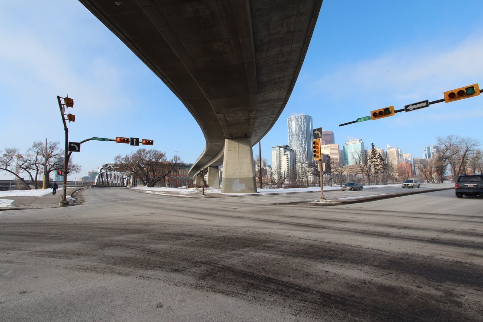 A curving concrete overpass sweeping over a road towards Calgary’s towers