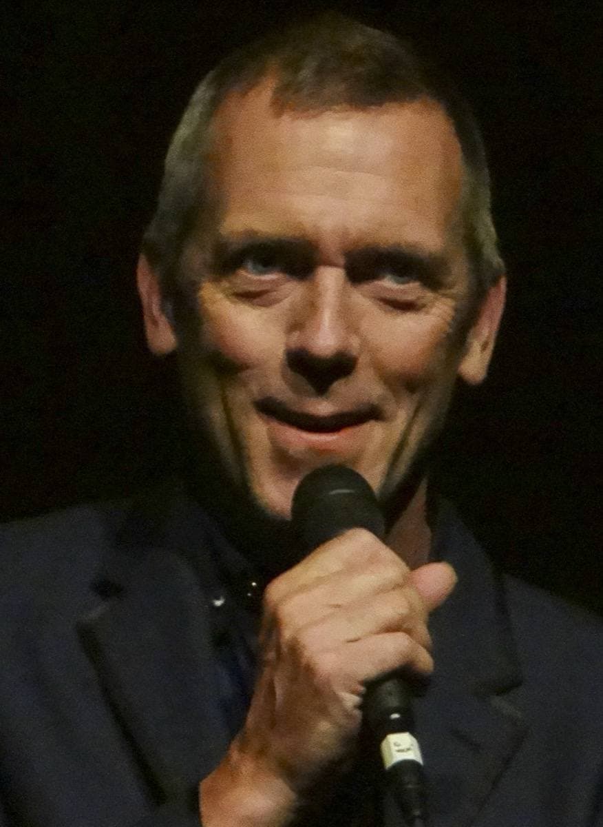 Hugh Laurie singing into a hand microphone, dark jacket
