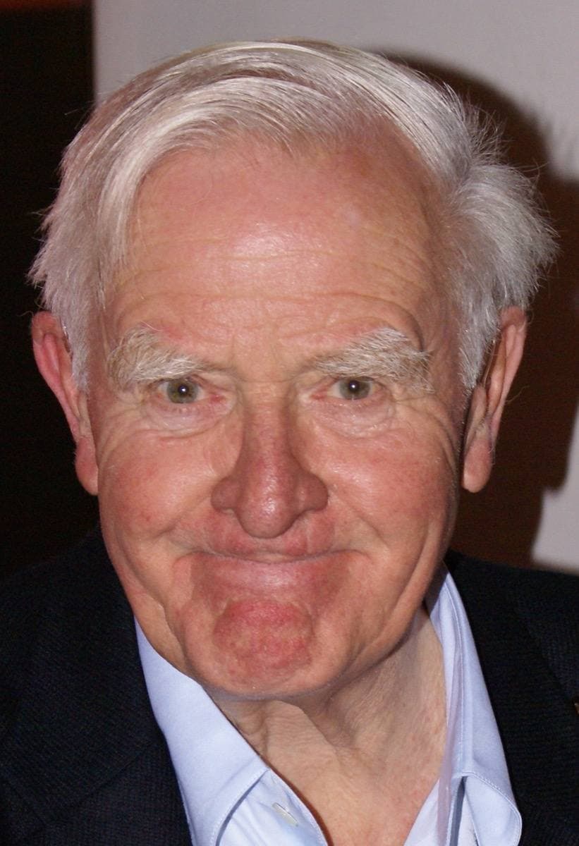 John le Carré, white-haired, in a grey jacket