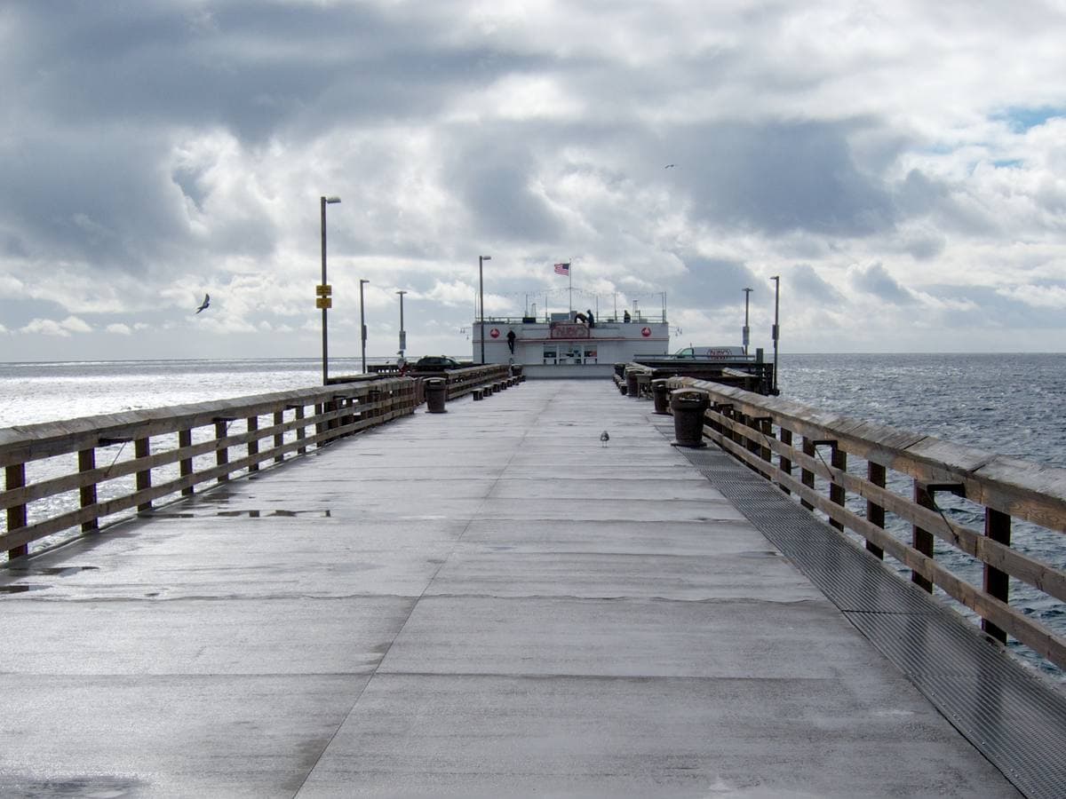 A long straight concrete pier deck with wooden rails under cloud