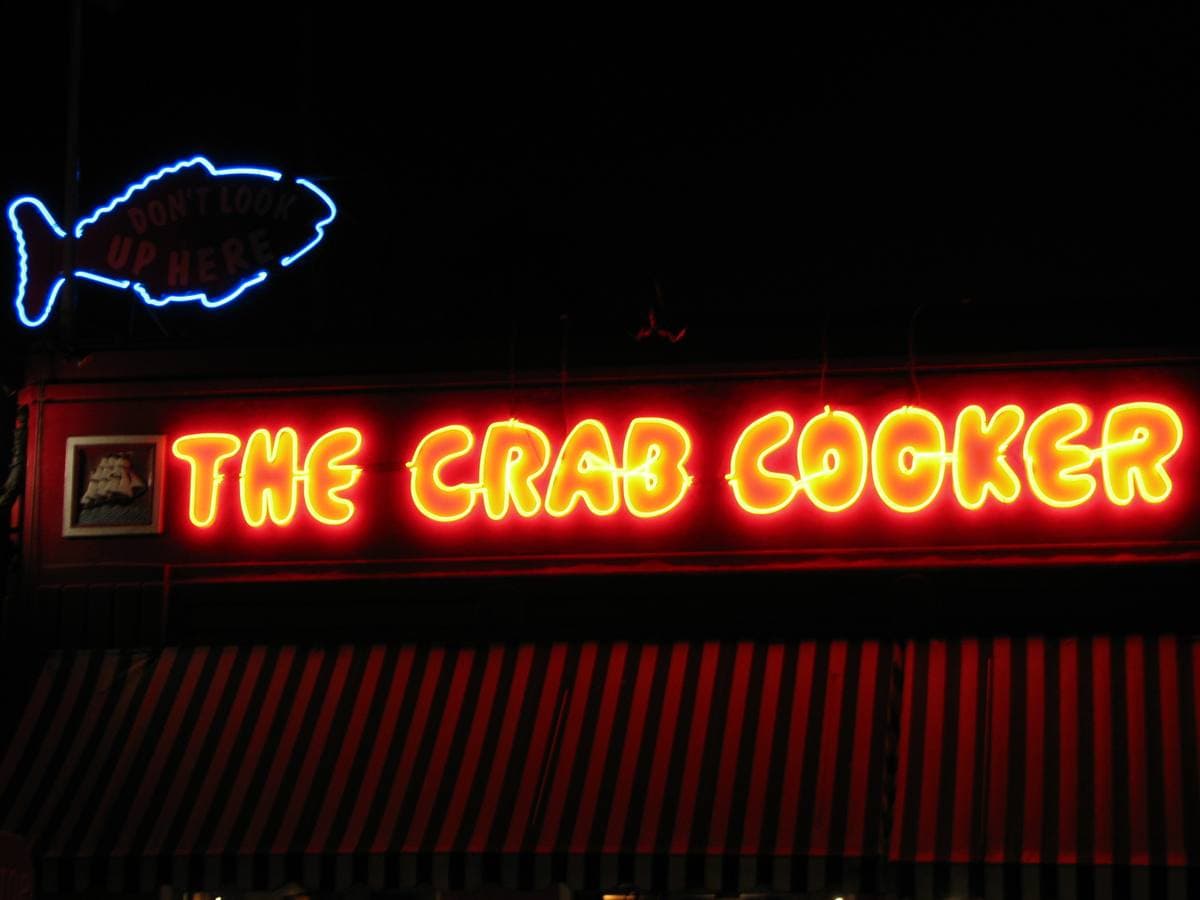 Red neon lettering reading THE CRAB COOKER beside a blue neon fish at night