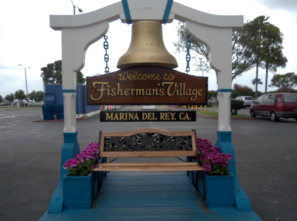 A white arch with a ship’s bell over a sign reading Welcome to Fisherman’s Village
