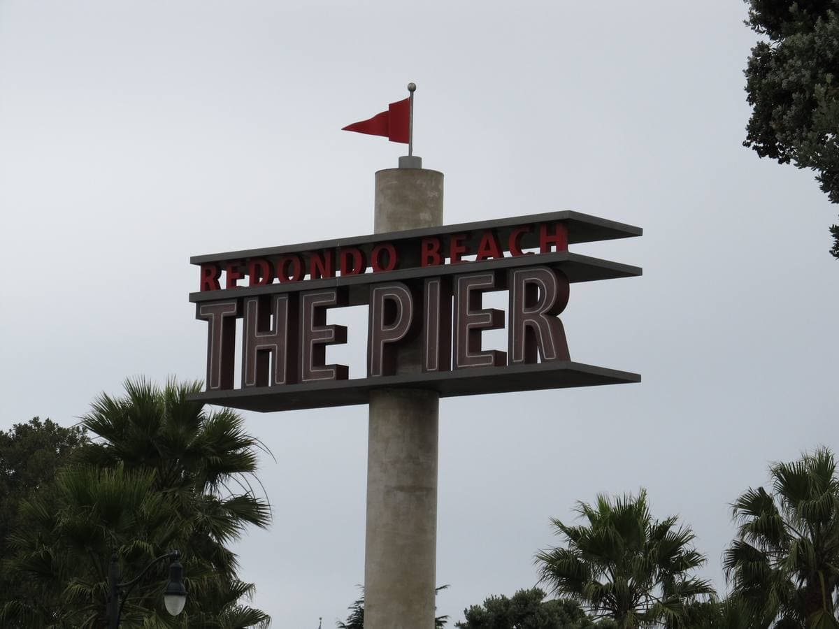 A tall sign reading THE PIER with a red flag against a grey sky