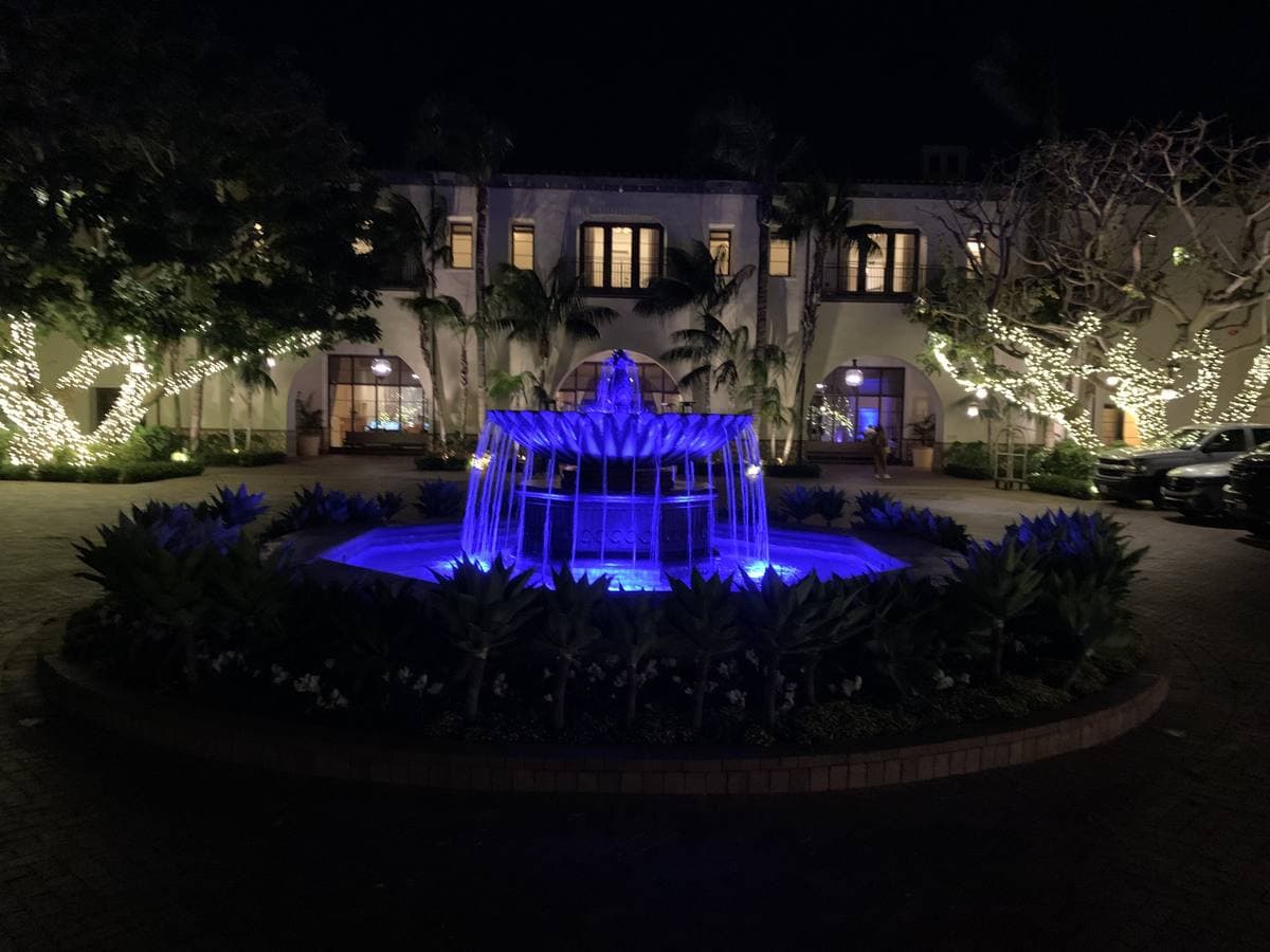A lit blue fountain in front of a resort building at night