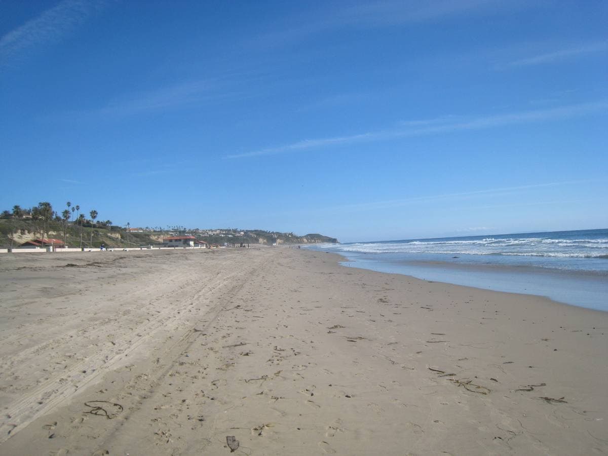A long sandy beach with low surf and hills behind