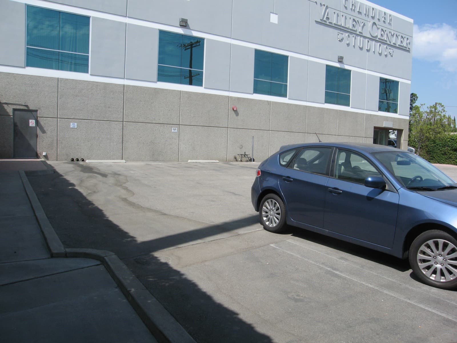 A grey studio building lettered Chandler Valley Center Studios over a parking lot with a blue car