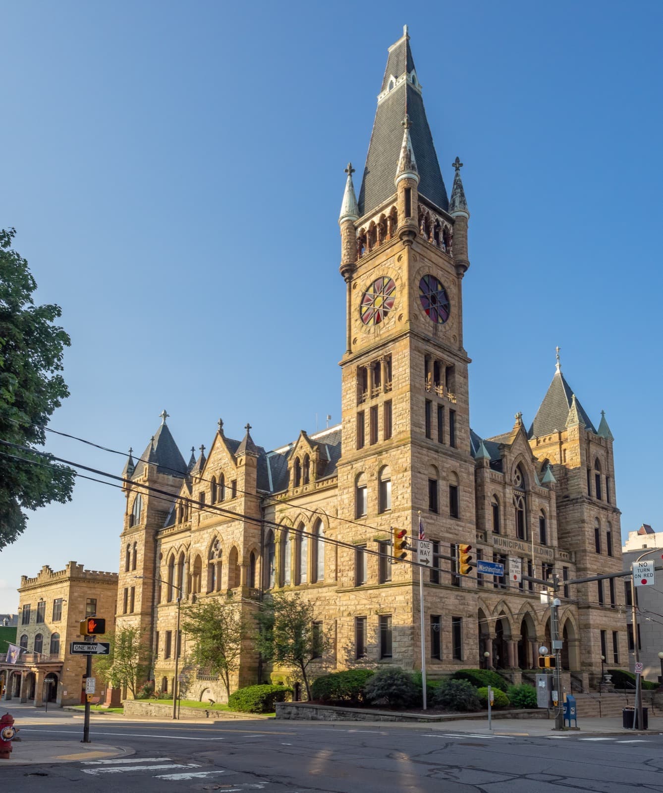 A Gothic stone city hall with a tall slate-roofed clock tower against blue sky