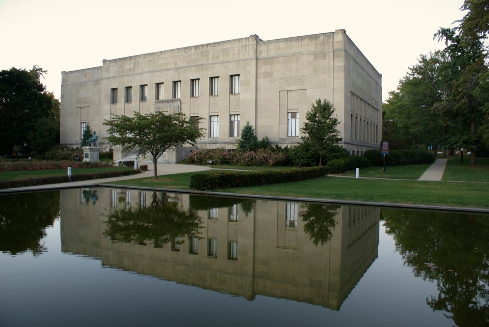 A pale stone museum front reflected in a long pool among trees