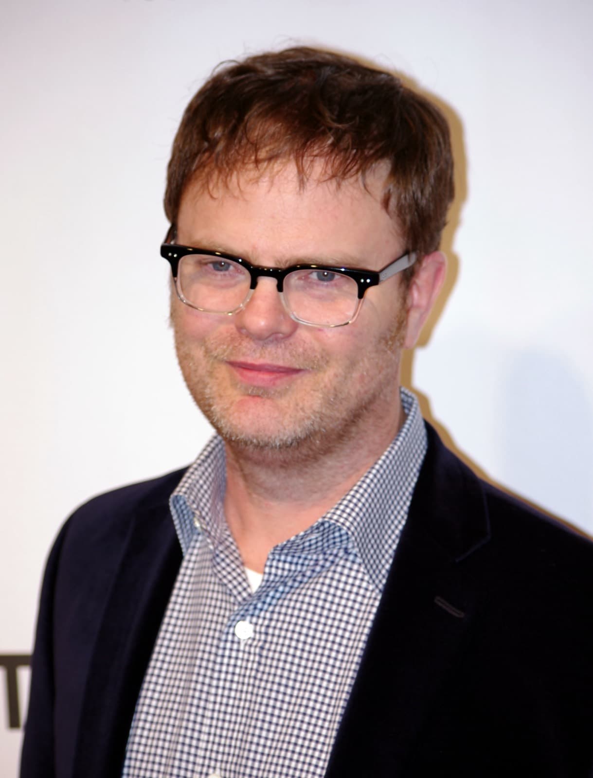 Rainn Wilson in black-rimmed glasses, a checked shirt and dark jacket