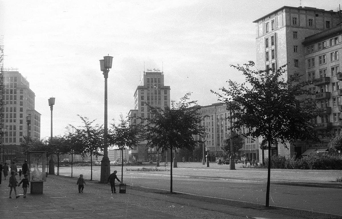 A wide East Berlin boulevard lined with tall tiled apartment blocks in 1962, a few cars on the road