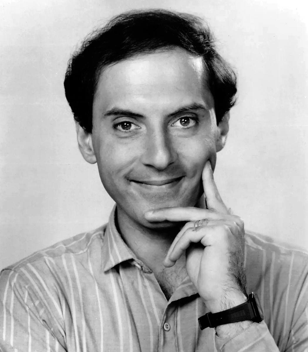 Black-and-white press portrait of a young Dan Castellaneta, smiling, with dark curly hair