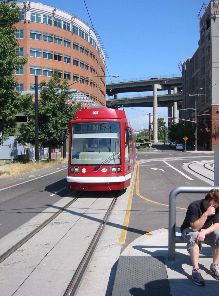 A red streetcar on tracks at a stop, with a curved office block behind