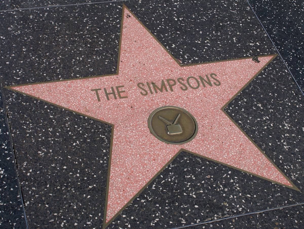 A pink terrazzo star on a dark pavement reading THE SIMPSONS above a television emblem