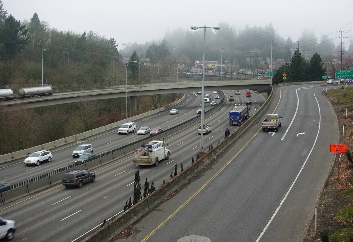 A six-lane highway curving through wooded hills in mist