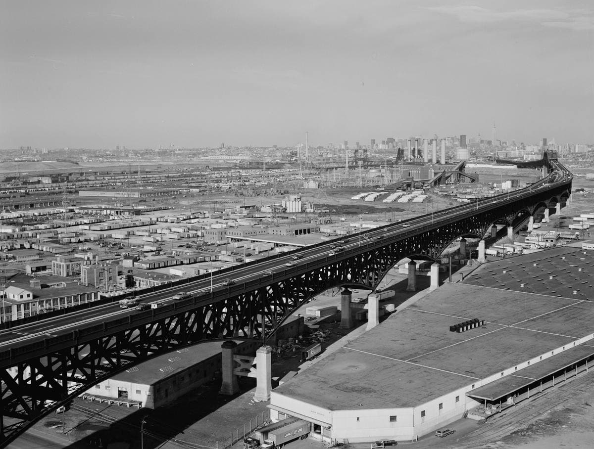 A black steel viaduct crossing flat industrial land towards a distant skyline