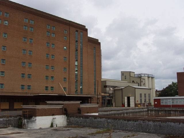 A long brick brewery block and silos behind a fenced yard