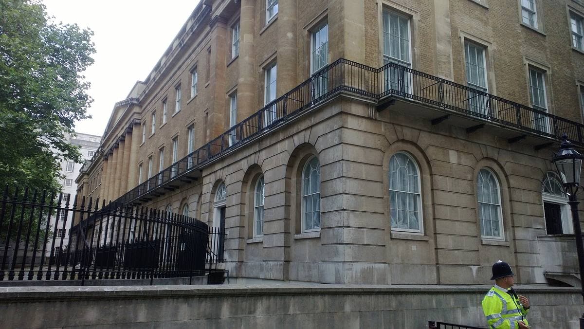 A stone terrace of tall windows behind black railings, a police officer at its foot