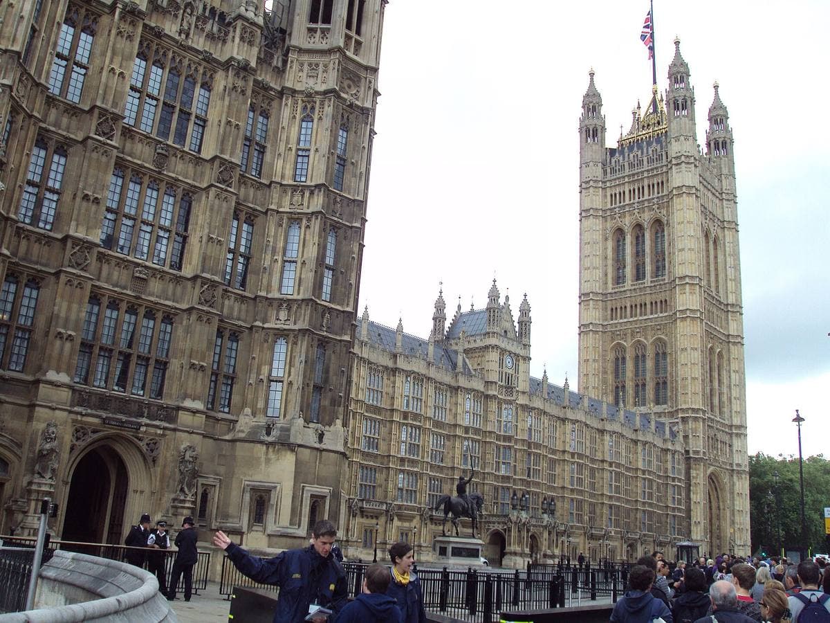The Victoria Tower and the Gothic front of the Palace of Westminster above a crowd on St Margaret Street