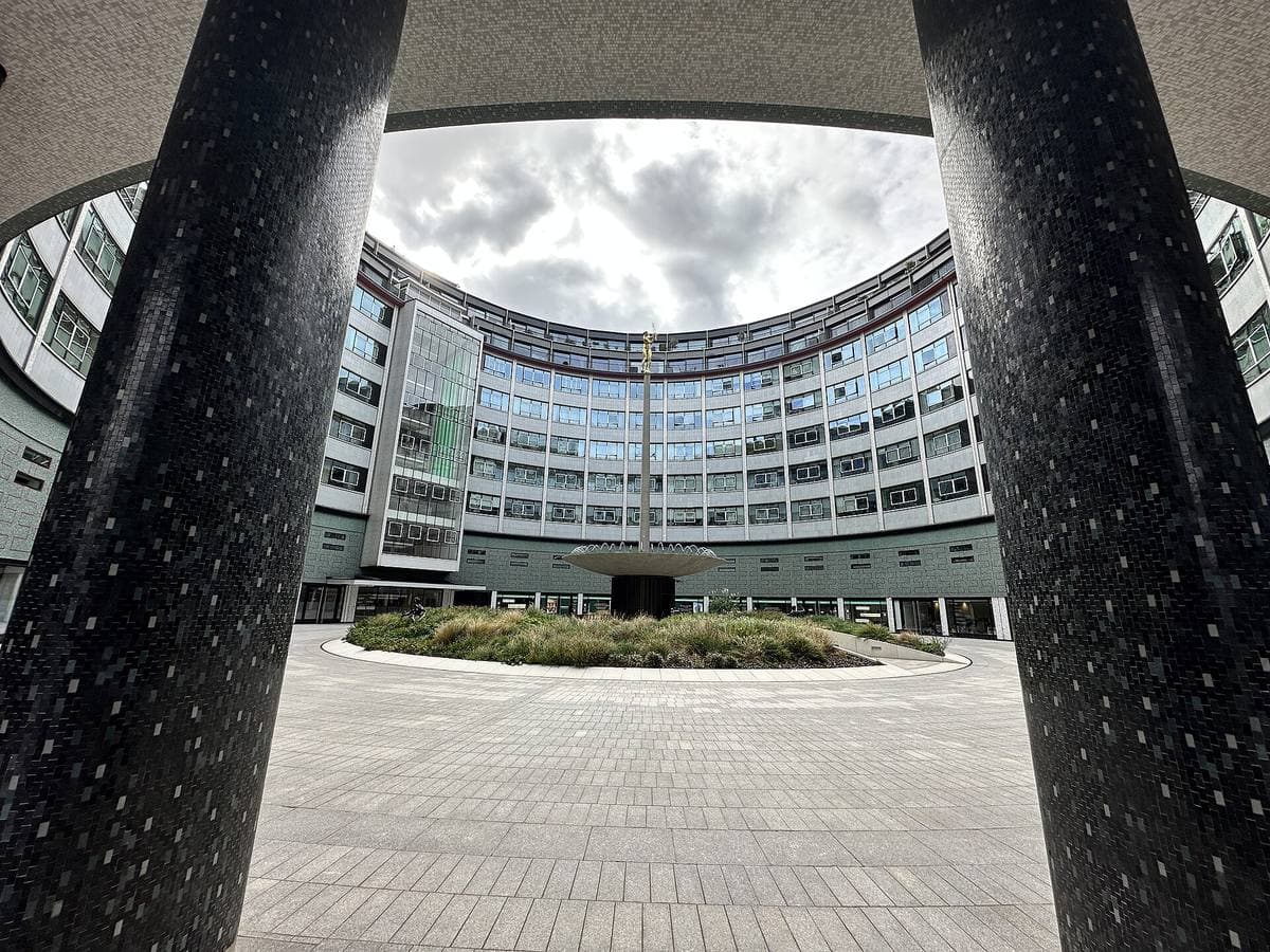The curved glass ring of Television Centre round a paved courtyard, seen between two dark columns