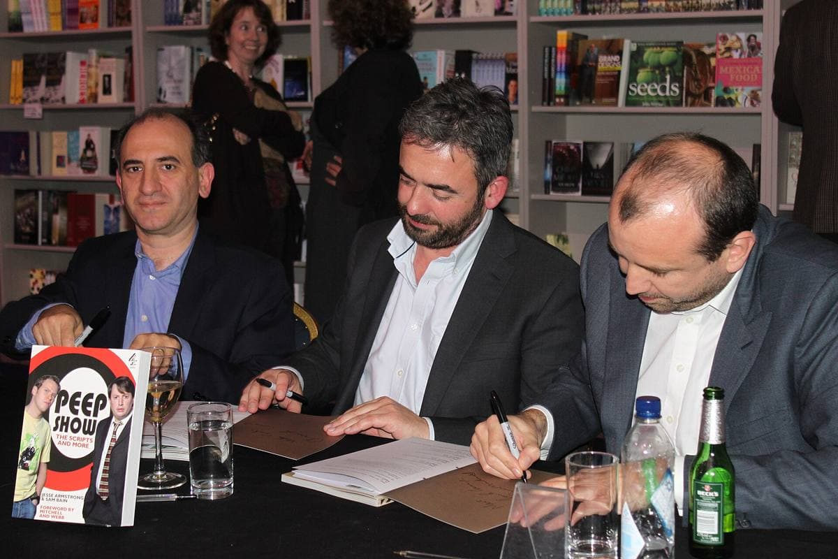 Three men signing books at a table in front of shelves