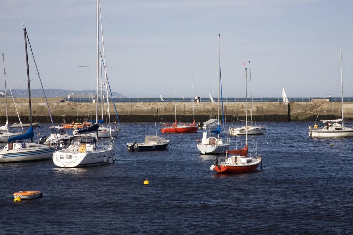 Small boats moored in a harbour under a pale sky, a harbour wall beyond