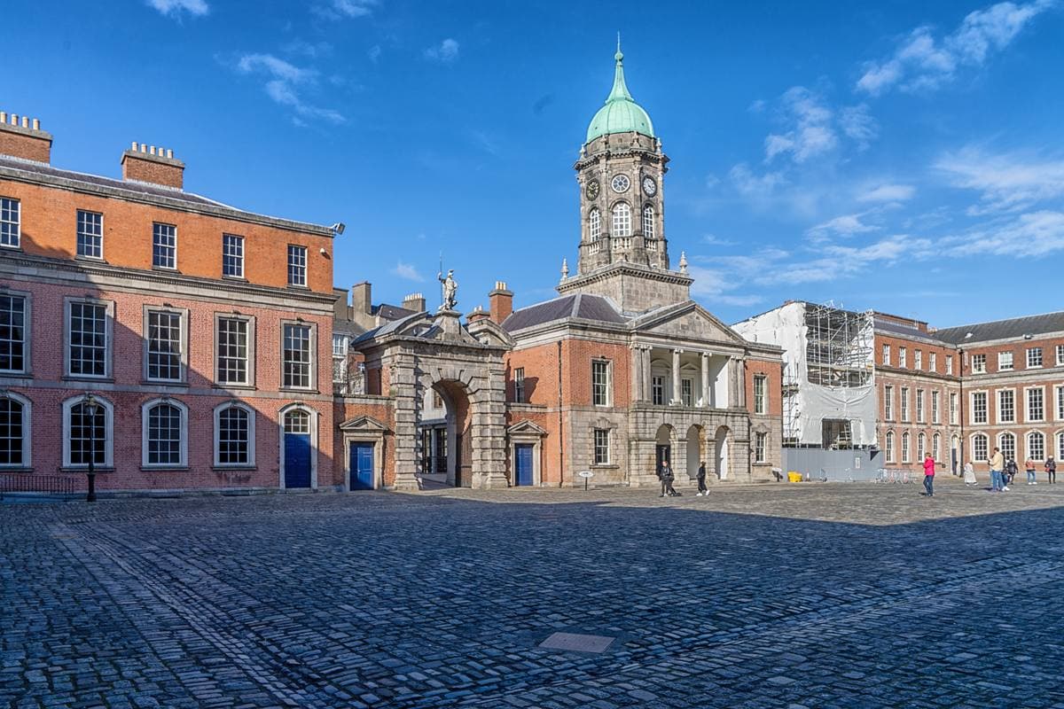 A cobbled courtyard enclosed by red-brick buildings with a green-domed tower in the middle