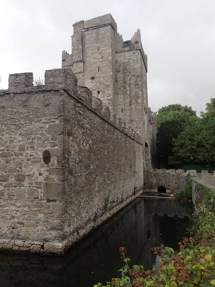 A tall stone castle wall dropping straight into a green moat