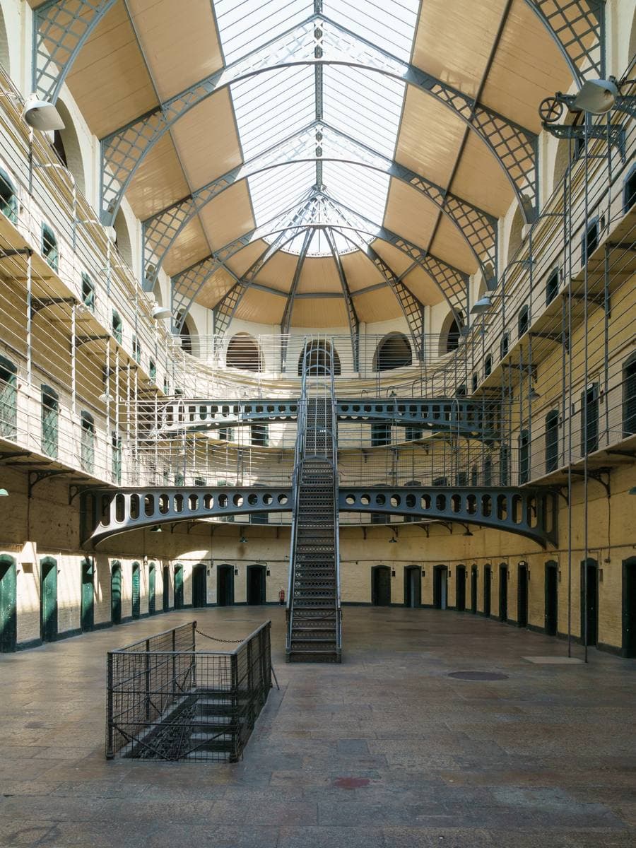 A long Victorian prison hall with three tiers of cell doors, iron walkways and a glass roof