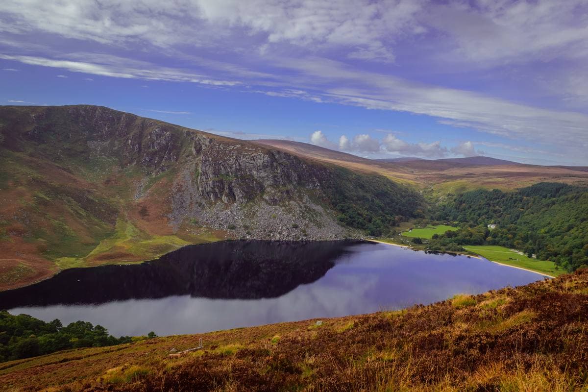 A dark lake between steep brown and green hills, a pale beach at its far end