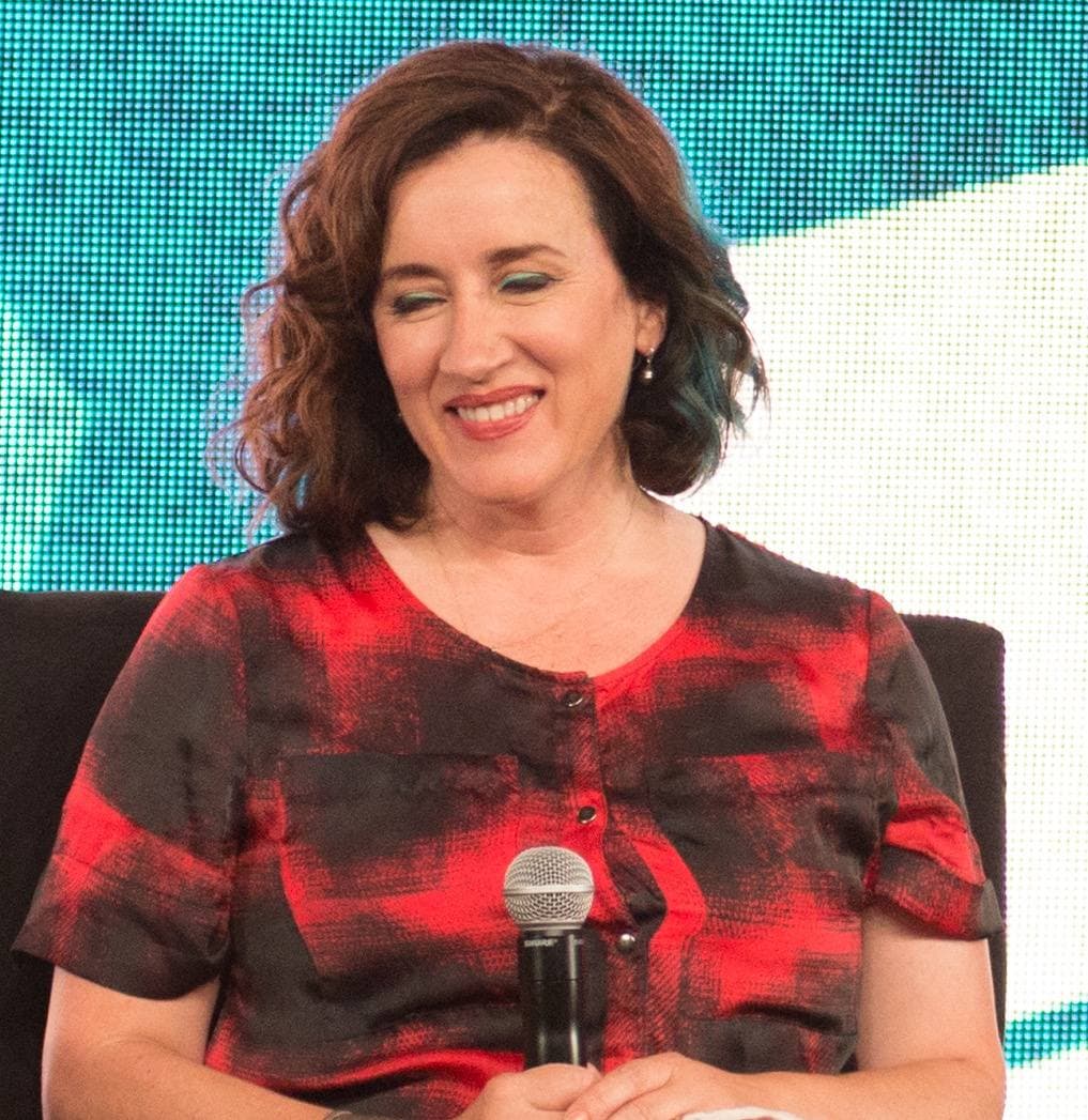 Maria Doyle Kennedy smiling at a panel, in a red and black checked shirt