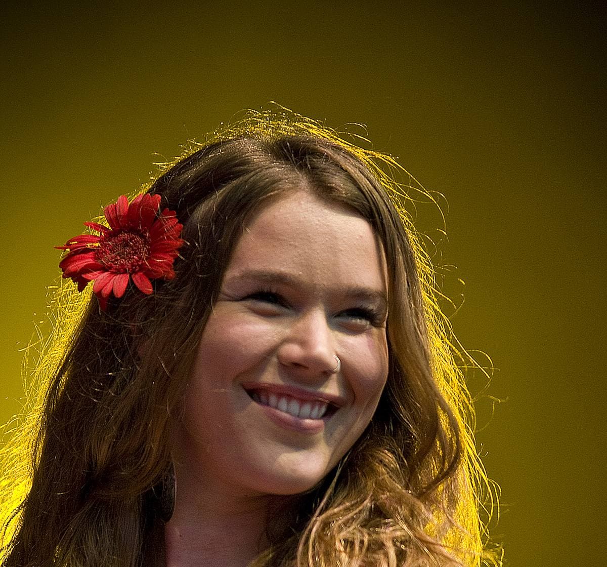 Joss Stone on stage with a red flower in her long hair, smiling