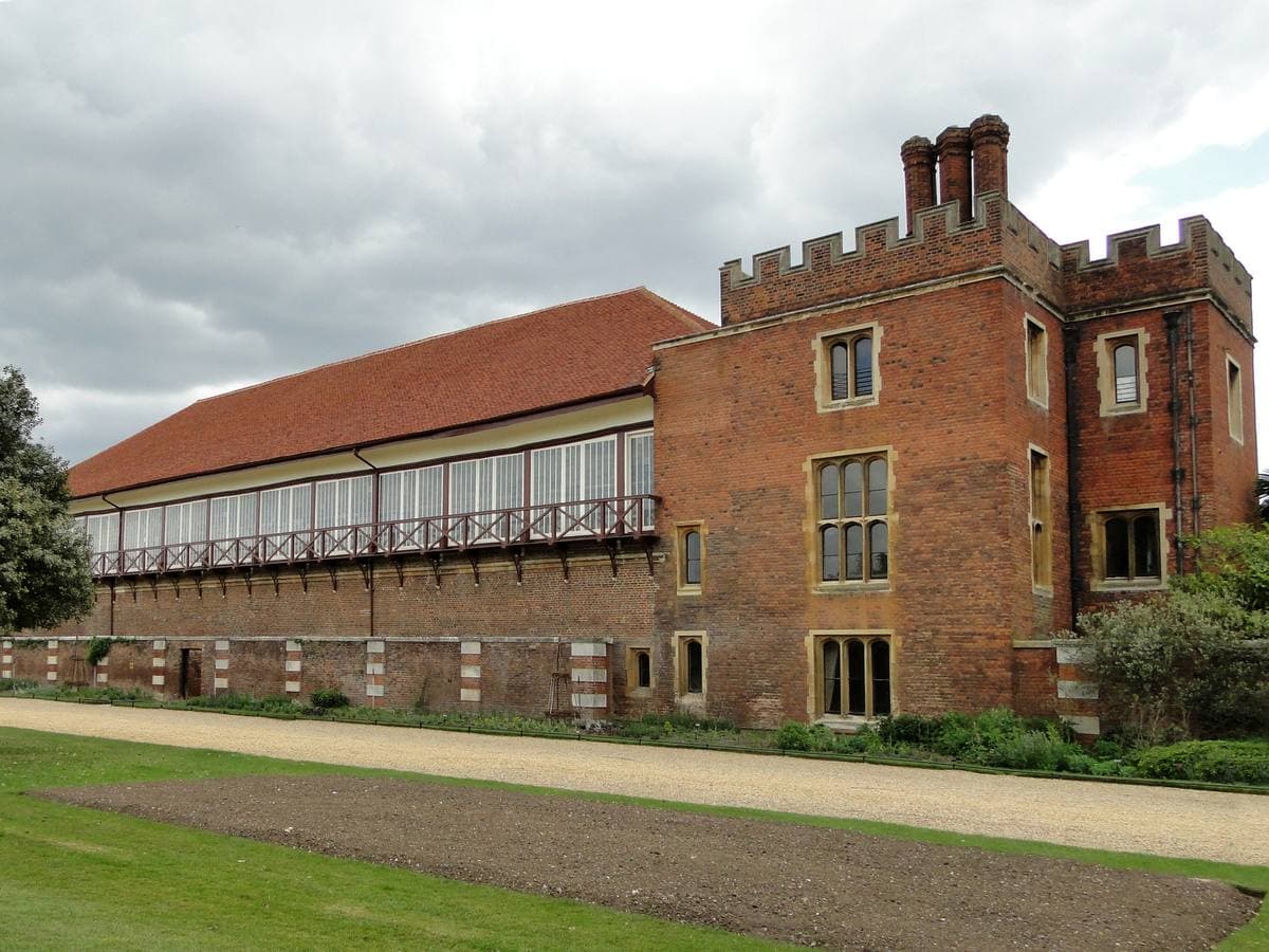 A long red-brick building with tall windows and a battlemented end, a lawn in front