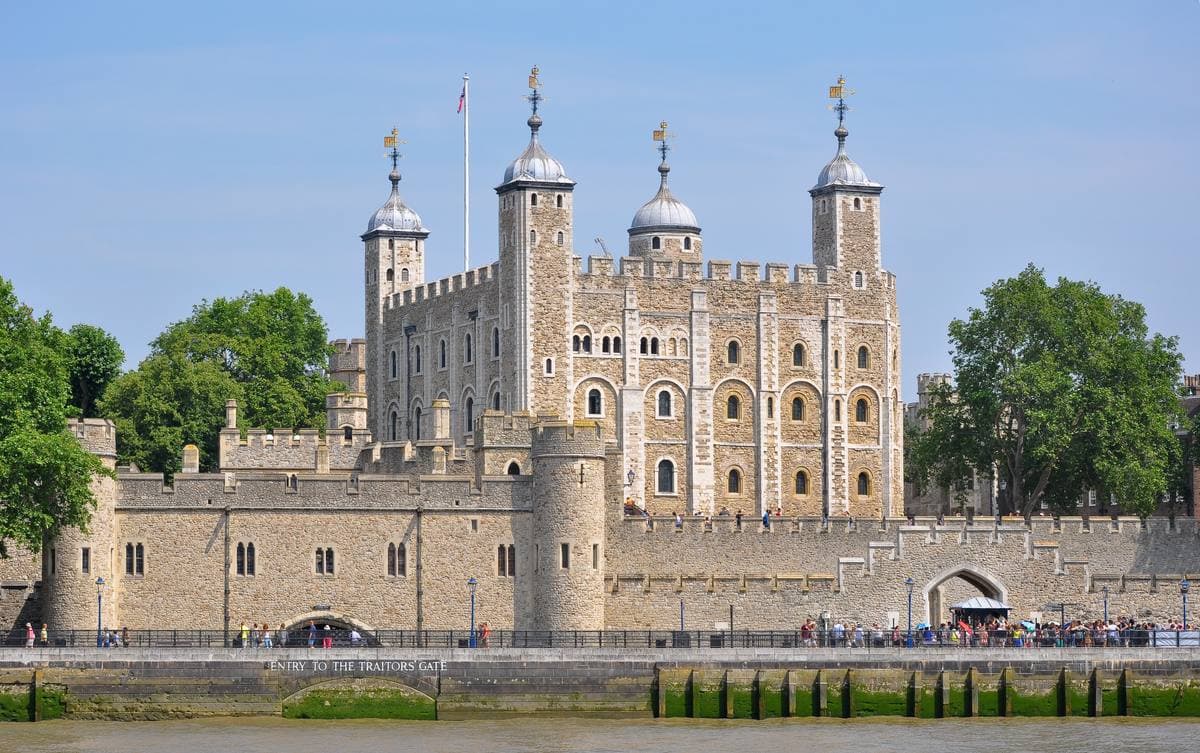The pale stone White Tower with four turrets rising behind the Tower's outer walls by the river