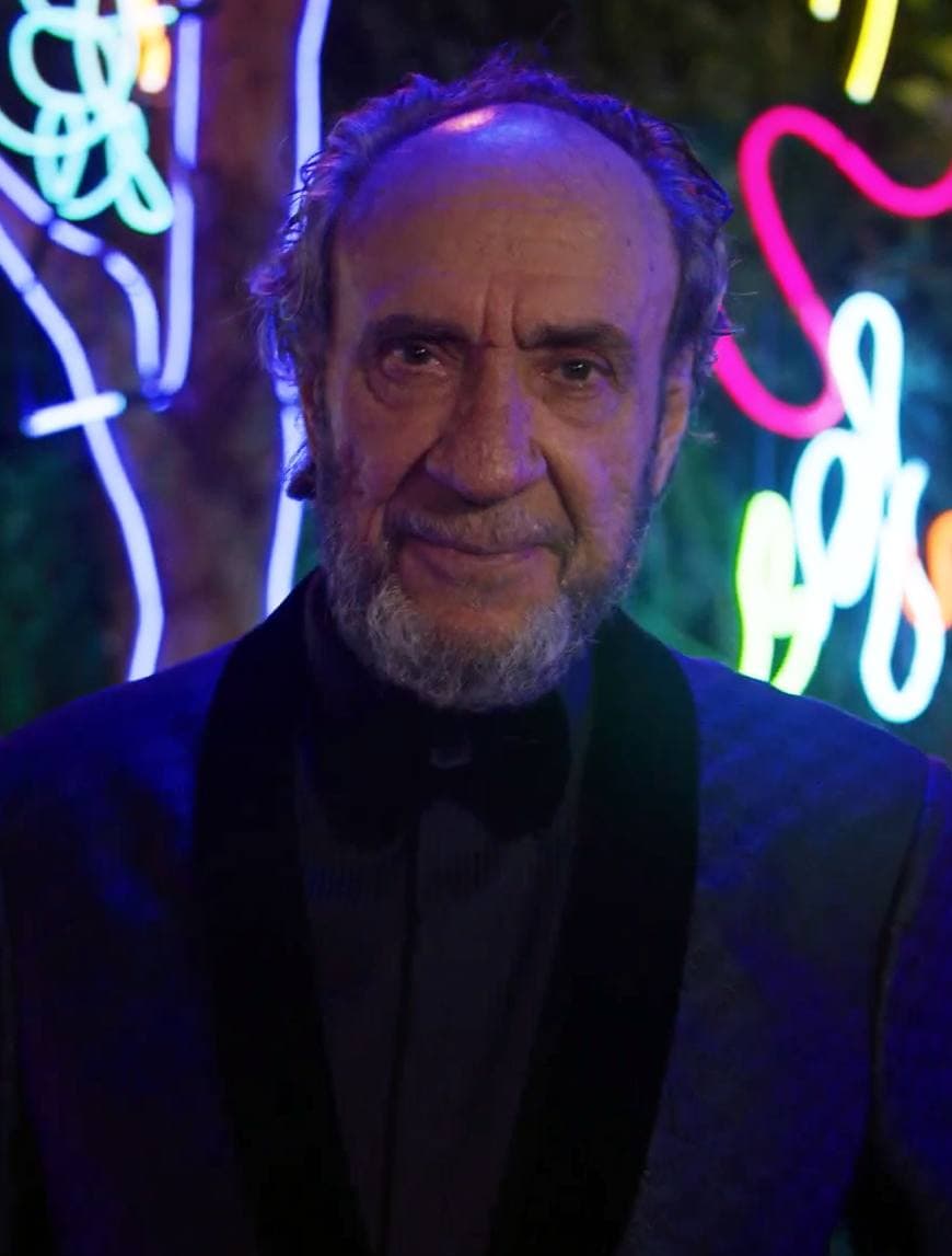 F. Murray Abraham in a dark dinner jacket in front of neon garden lights