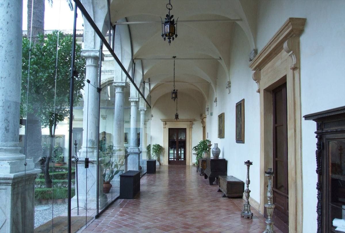 A long vaulted cloister corridor with terracotta floor, lanterns and carved wooden furniture