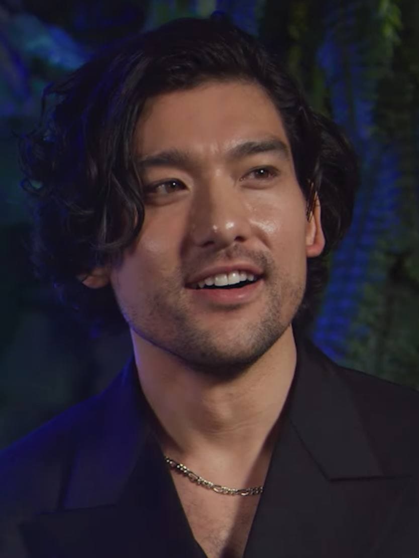 Will Sharpe smiling, in a dark open-necked shirt