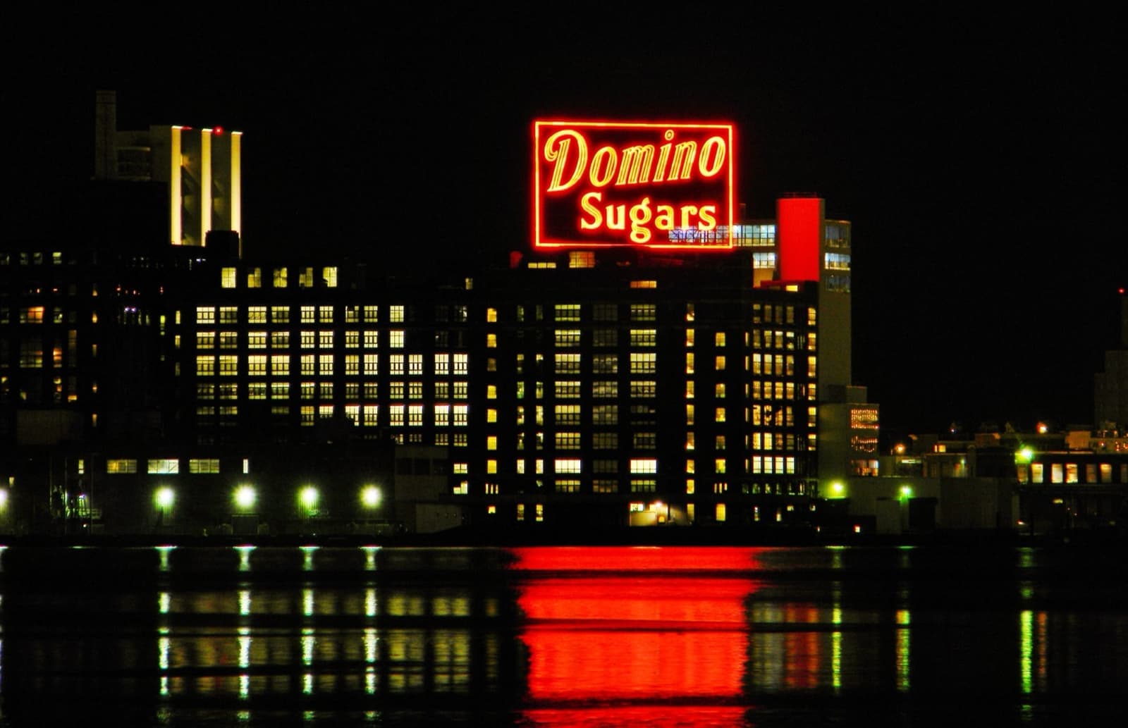 A red neon Domino Sugars sign reflected in dark harbour water