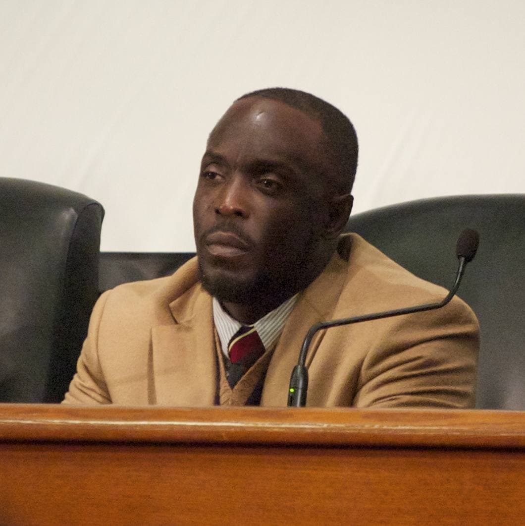 Michael K. Williams in a camel jacket and tie at a panel microphone