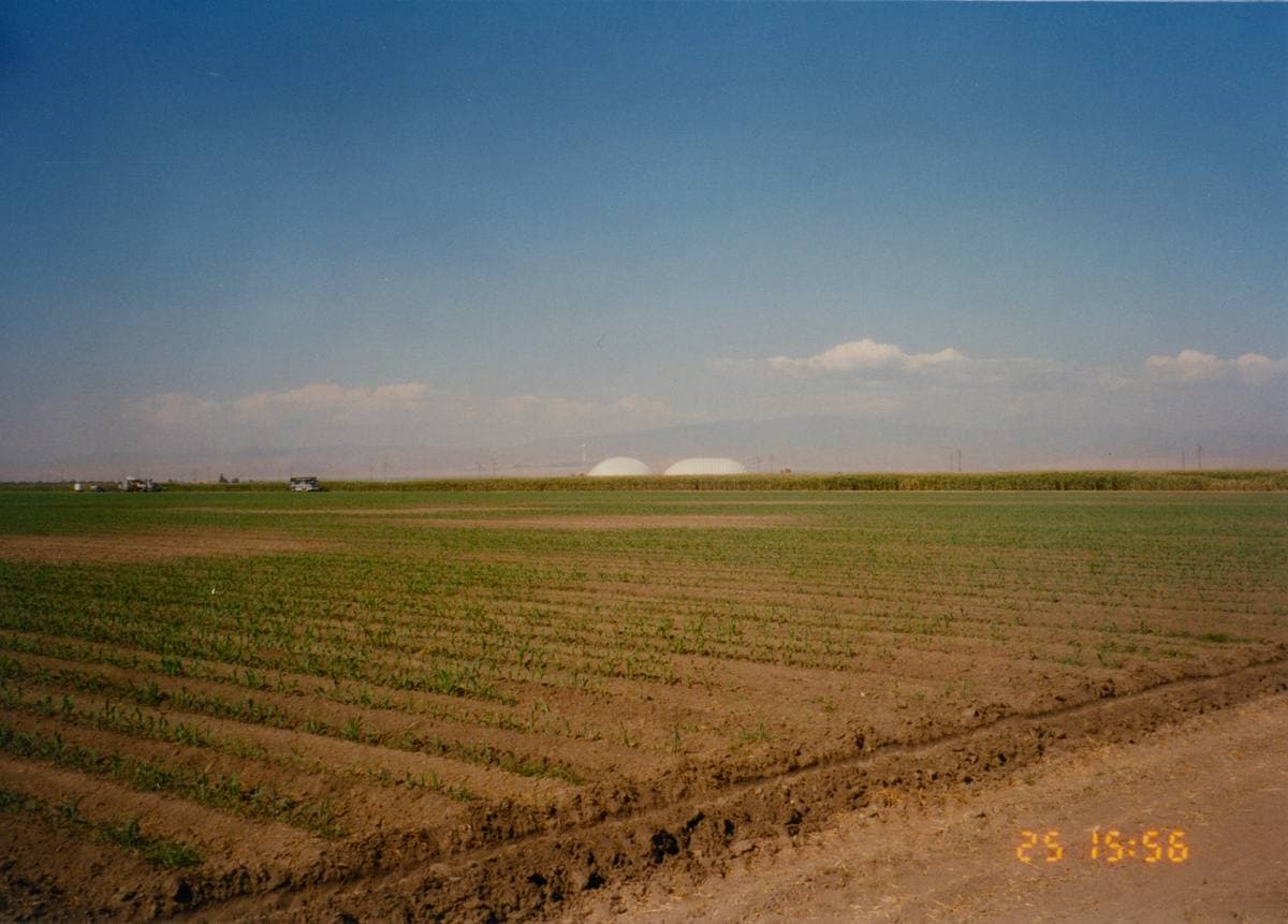 Flat ploughed farmland under a pale sky, with two low white domes on the horizon