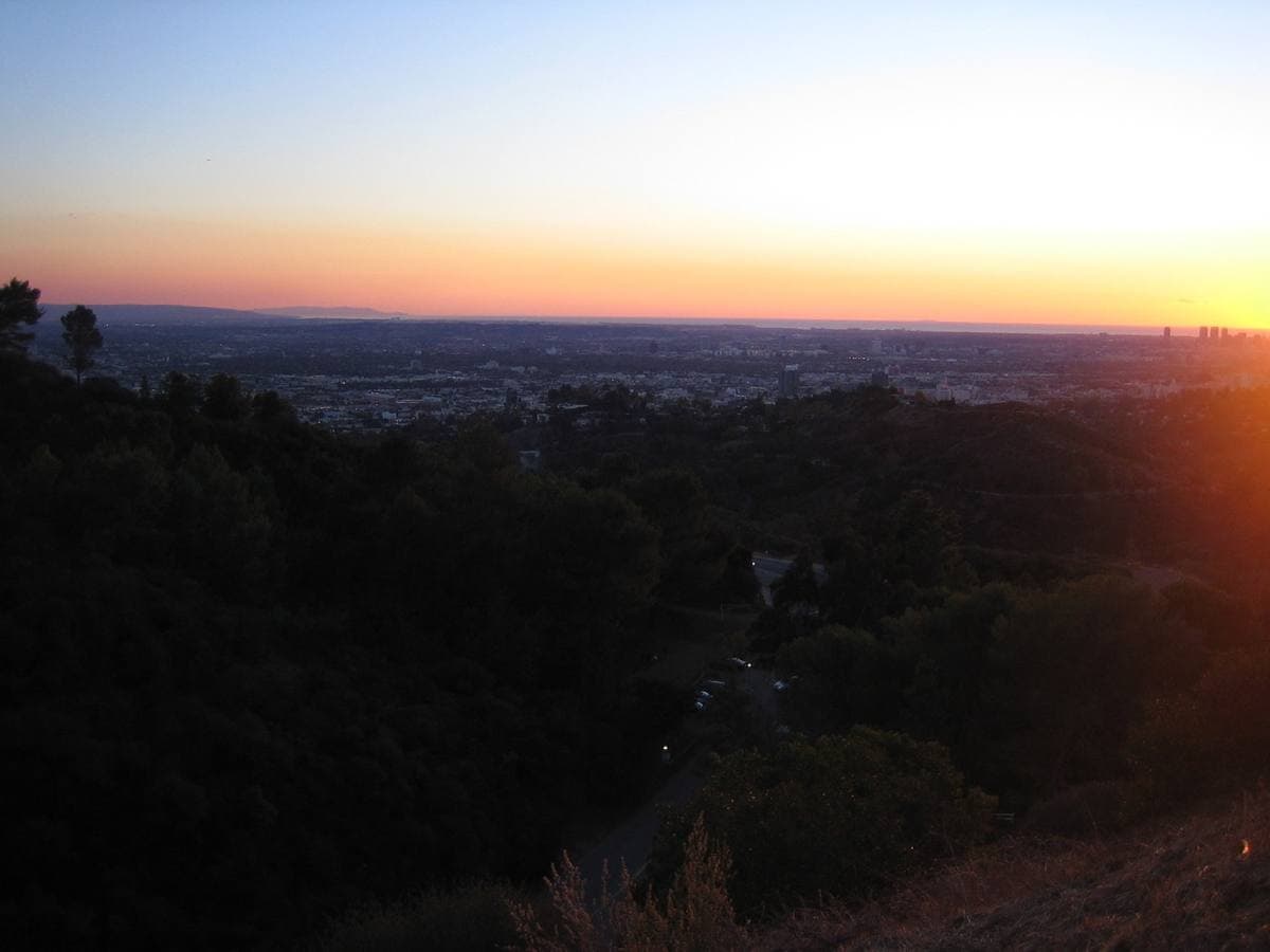 Dark wooded hills of Griffith Park with the lights of Los Angeles under an orange sunset